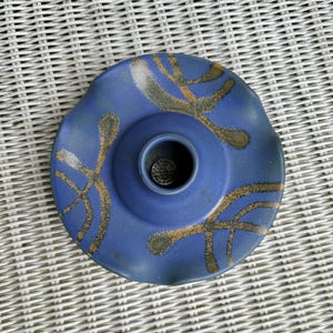 May include: Blue ceramic vase with a wavy rim and gold abstract designs. The vase has a small hole in the centre for flowers.