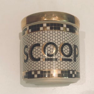May include: A white ceramic jar with a gold lid and black and gold geometric pattern. The jar has the word "SCOOP" written on it in black letters.