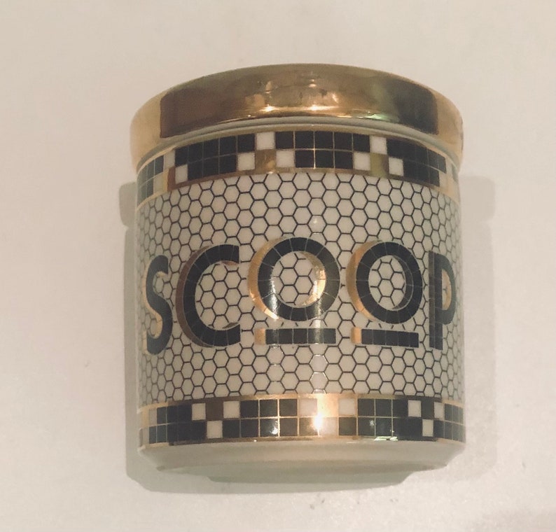 May include: A white ceramic jar with a gold lid and black and gold geometric pattern. The jar has the word "SCOOP" written on it in black letters.