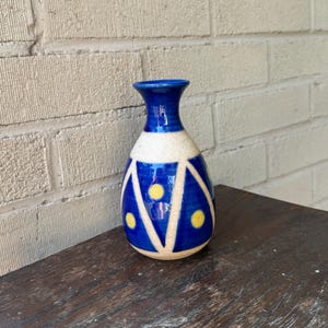 May include: A small blue and white ceramic vase with yellow polka dots. The vase has a geometric design with triangles and a rounded base.
