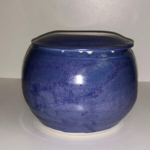 May include: A small, round ceramic jar with a lid. The jar is a deep blue color with a white rim. The lid is also blue with a white rim.