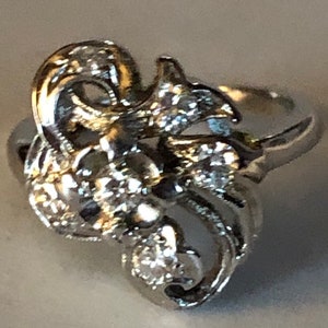 May include: A silver ring with a floral design and clear stones. The ring is intricate and detailed, with a delicate band.