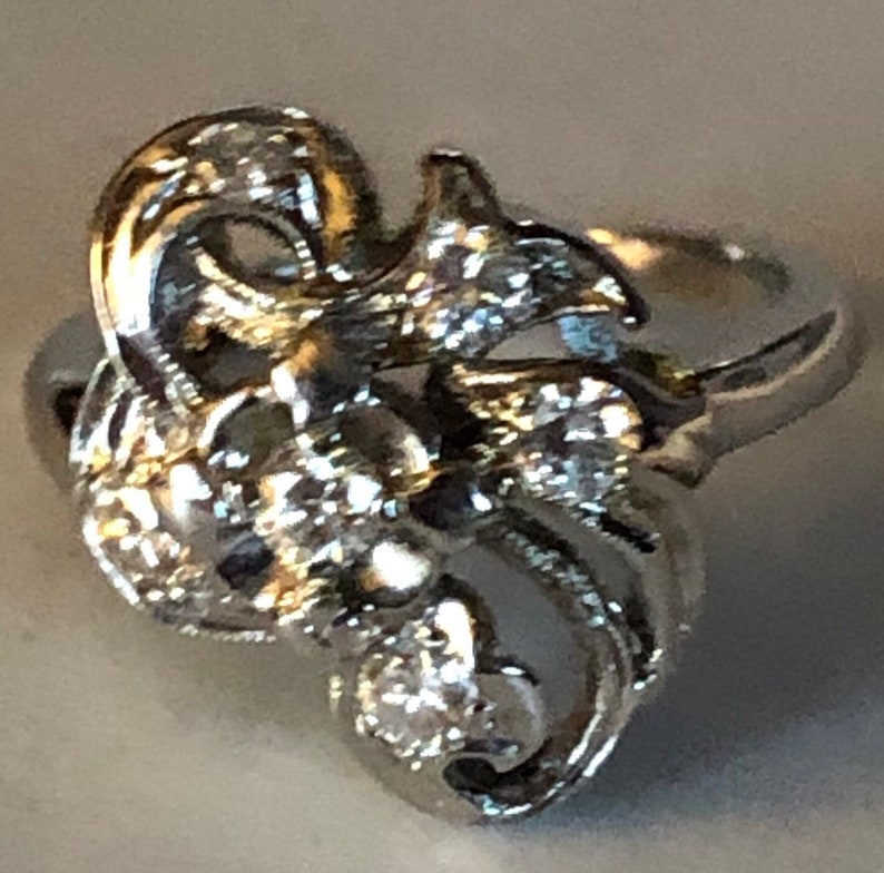 May include: A silver ring with a floral design and clear stones. The ring is intricate and detailed, with a delicate band.