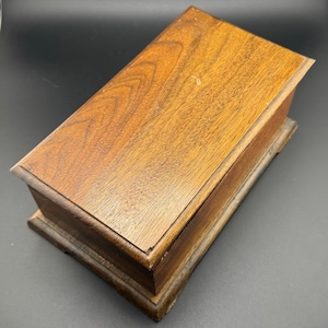 May include: A wooden box with a hinged lid and a simple design. The box is made of dark brown wood with a smooth finish.