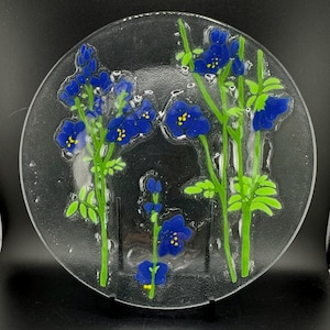 Puede incluir: Un plato de vidrio transparente con un diseño floral azul y verde. Las flores están pintadas en el vidrio y tienen una textura en relieve.