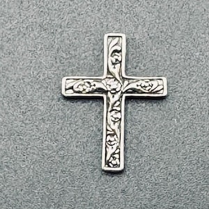 May include: A silver cross pendant with an ornate floral design.