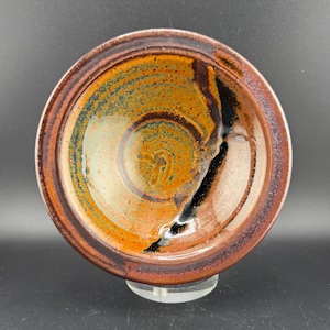 May include: A ceramic bowl with a brown, orange, and black glaze. The bowl has a swirling pattern and a raised rim.