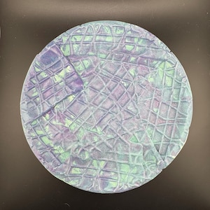 Puede incluir: Un plato redondo de cerámica texturizado con un esmalte azul y verde. El plato tiene un patrón de cuadrícula y un acabado craquelado.