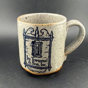 Peut inclure: Une tasse en céramique tachetée avec une anse. La tasse présente une illustration bleue d'un motif encadré avec le texte "Jas. Townsend & Son, Inc.". La tasse a un schéma de couleurs beige et marron.