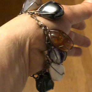 Pode incluir: Um bracelete de corrente de prata com v&aacute;rios pingentes em forma de cora&ccedil;&atilde;o de pedras preciosas. Os pingentes s&atilde;o de v&aacute;rias cores, incluindo branco, cinza, &acirc;mbar e roxo.