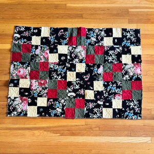 Op de afbeelding: Een patchworkdeken met een geruit patroon in zwart, wit, rood en groen. De deken is gemaakt van bloemenstof met verschillende patronen.