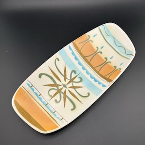 May include: A rectangular ceramic dish with a white background and a colorful geometric design. The design features blue, green, gold, and orange colors. The dish is perfect for serving snacks or appetizers.