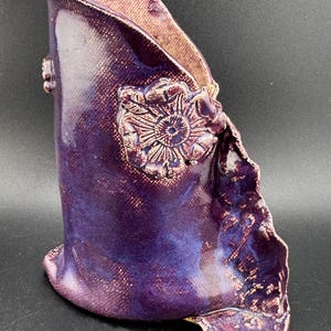 May include: A purple ceramic vase with a textured surface and a raised floral design. The vase has a unique, asymmetrical shape.