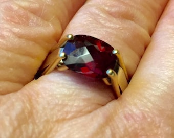 May include: A gold ring with a large, oval-shaped, red gemstone.
