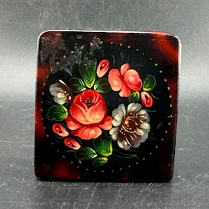 May include: Square, hand-painted trinket box with a floral design. The box features a dark background with a red and brown tortoiseshell pattern around the edges. The floral design includes red roses, white flowers, and green leaves.