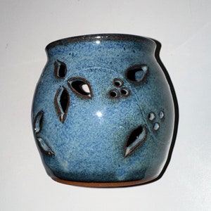 Puede incluir: Un portavelas de cerámica azul con un diseño decorativo de hojas y bayas recortadas. El portavelas tiene un acabado esmaltado y una forma redondeada.