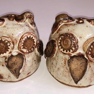 Könnte beinhalten: Zwei Salz- und Pfefferstreuer aus Keramik in Form von Eulen mit brauner und weißer Glasur. Die Eulen haben große braune Augen und braune Schnäbel.