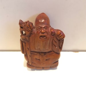 May include: A small, intricately carved wooden figurine of a Chinese deity holding a staff with a dragon head. The figurine is brown and has a detailed face with a long beard.