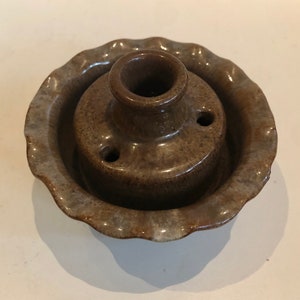 May include: A brown ceramic inkwell with a scalloped edge and three holes in the top. The inkwell is glazed in a brown and gray color.