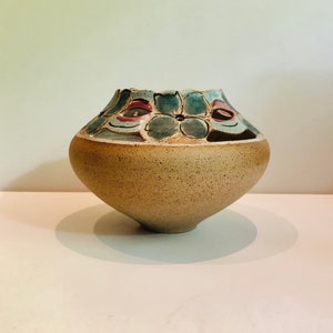 May include: A ceramic vase with a brown speckled glaze and a decorative design of blue and pink flowers. The vase has a wide opening and a rounded bottom.