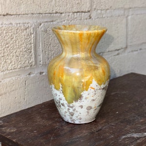 May include: A small, yellow and white ceramic vase with a speckled glaze. The vase has a rounded body and a flared opening.
