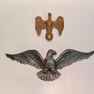 Puede incluir: Dos piezas de decoración de pared de águila de metal. Un águila es dorada y tiene las alas extendidas. La otra águila es plateada y tiene las alas extendidas.