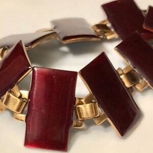 Peut inclure: Un bracelet en or et bordeaux avec des maillons rectangulaires. Les maillons sont reli&eacute;s par des charni&egrave;res dor&eacute;es.