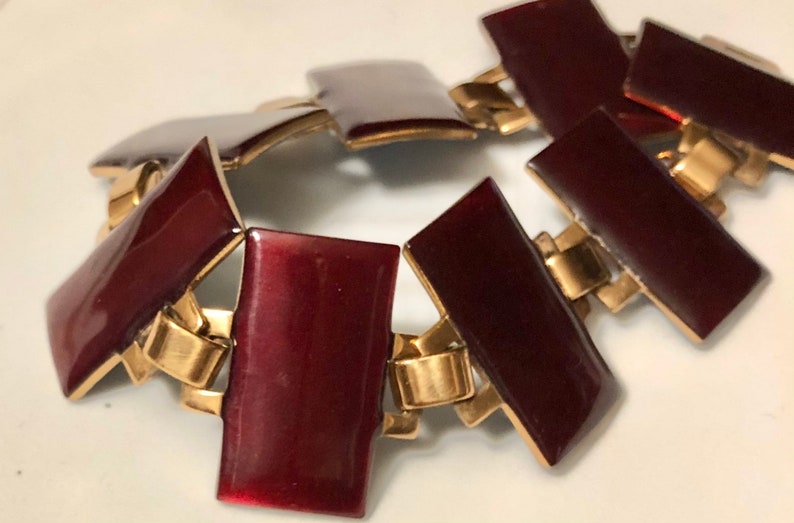 Peut inclure: Un bracelet en or et bordeaux avec des maillons rectangulaires. Les maillons sont reli&eacute;s par des charni&egrave;res dor&eacute;es.