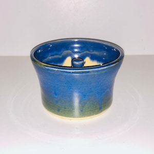 May include: A blue and green ceramic bowl with a white centre and a small knob in the centre. The bowl is glazed and has a rustic look.