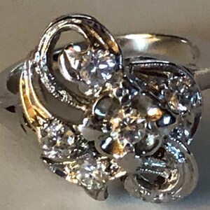 May include: A silver ring with a large, intricate design featuring multiple small diamonds. The ring has a delicate, feminine style.