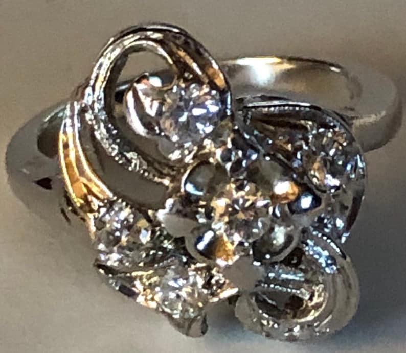 May include: A silver ring with a large, intricate design featuring multiple small diamonds. The ring has a delicate, feminine style.