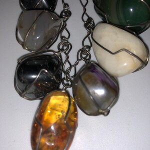 Pode incluir: Um bracelete de corrente de prata com sete pedras de diferentes cores, cada uma envolta em arame. As pedras incluem &acirc;mbar, ametista, &aacute;gata, verde, preto e branco.