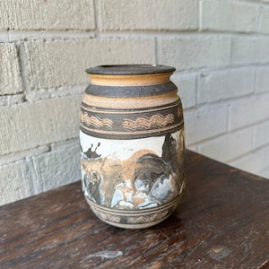 Könnte beinhalten: Eine braune und weiße Keramikvase mit geometrischem Muster und einem Tiermotiv. Die Vase hat eine abgerundete Form und eine breite Öffnung.