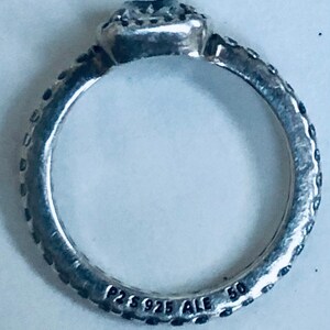 May include: Silver ring with a square-shaped stone set in a bezel setting. The ring band is textured and has the inscription "P2S 925 ALE 50" on the inside.