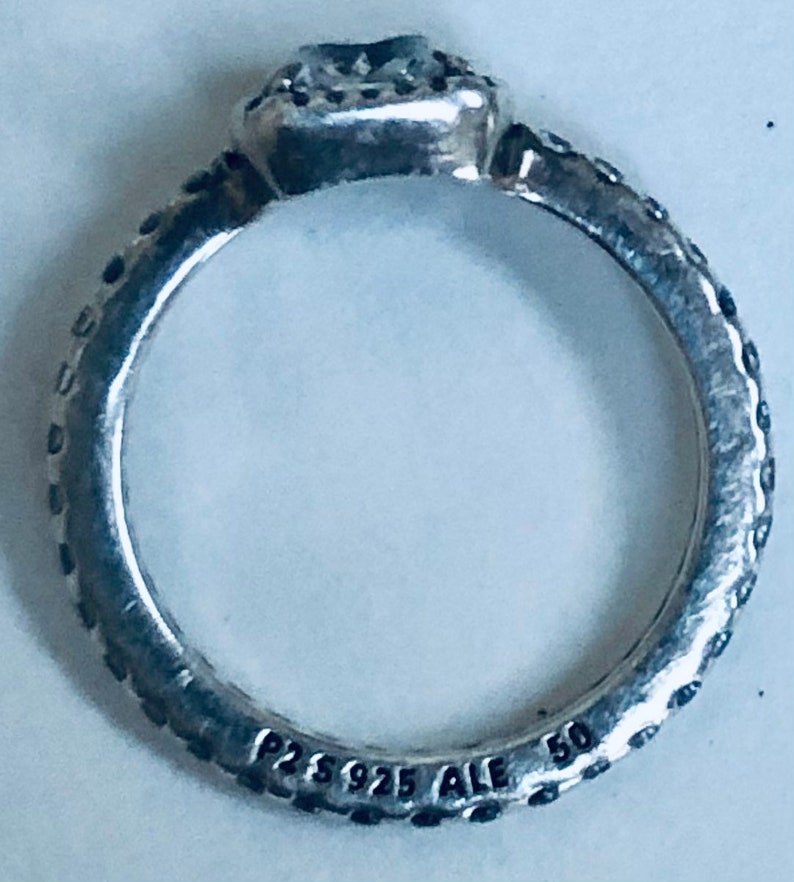 May include: Silver ring with a square-shaped stone set in a bezel setting. The ring band is textured and has the inscription "P2S 925 ALE 50" on the inside.