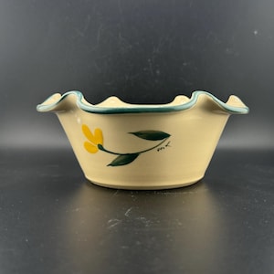 May include: A ceramic bowl with a scalloped rim and a green and yellow floral design. The bowl is hand-painted with a single yellow flower and green leaves.