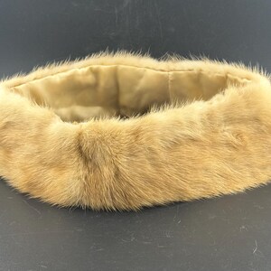 May include: A circular fur collar in light brown, featuring a soft, pale lining. The fur has a dense, plush texture. The collar is designed to be worn around the neck. The item is likely a fashion accessory.