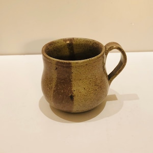 May include: A brown and tan ceramic mug with a speckled glaze. The mug has a rounded body and a handle.
