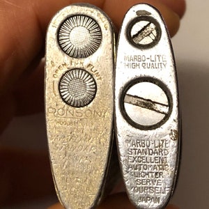 May include: Two silver lighters, one is a Ronson lighter with the text "OPEN FLINT RONSON GOODBRIDGE, N.J. USA" and the other is a Marbo-Lite lighter with the text "MARBO-LITE HIGH QUALITY MARBO-LITE STANDARD EXCELLENT AUTOMATIC LIGHTER SERVE YOURSELF JAPAN".