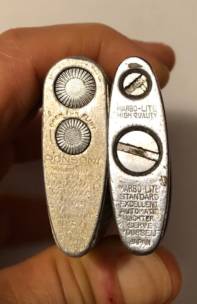 May include: Two silver lighters, one is a Ronson lighter with the text "OPEN FLINT RONSON GOODBRIDGE, N.J. USA" and the other is a Marbo-Lite lighter with the text "MARBO-LITE HIGH QUALITY MARBO-LITE STANDARD EXCELLENT AUTOMATIC LIGHTER SERVE YOURSELF JAPAN".