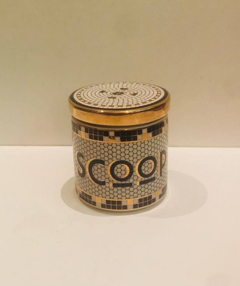 May include: A white ceramic jar with a gold lid and black and gold trim. The jar has a honeycomb pattern and the word "SCOOP" written in black letters with gold outlines.