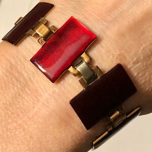 Peut inclure: Un bracelet en &eacute;mail rouge et bordeaux avec des maillons dor&eacute;s et argent&eacute;s. Le bracelet est compos&eacute; de pi&egrave;ces rectangulaires en &eacute;mail reli&eacute;es par des maillons m&eacute;talliques.