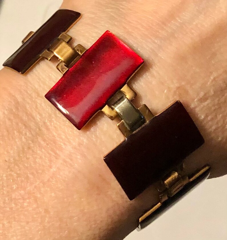 Peut inclure: Un bracelet en &eacute;mail rouge et bordeaux avec des maillons dor&eacute;s et argent&eacute;s. Le bracelet est compos&eacute; de pi&egrave;ces rectangulaires en &eacute;mail reli&eacute;es par des maillons m&eacute;talliques.