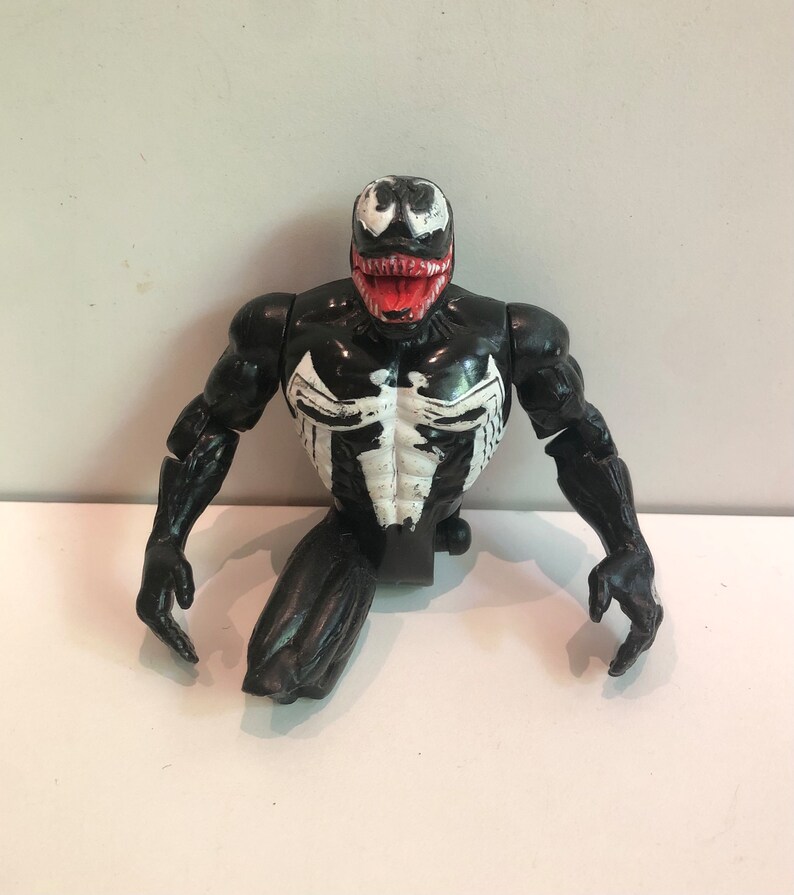 May include: Black and white Venom action figure with a red mouth. The figure is in a crouching pose with its arms outstretched.