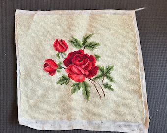 May include: A white canvas with a red rose and green leaves embroidered on it. The canvas is surrounded by a white border.