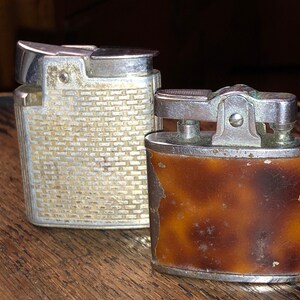 May include: Two vintage lighters, one silver with a textured design and one brown with a tortoiseshell pattern.
