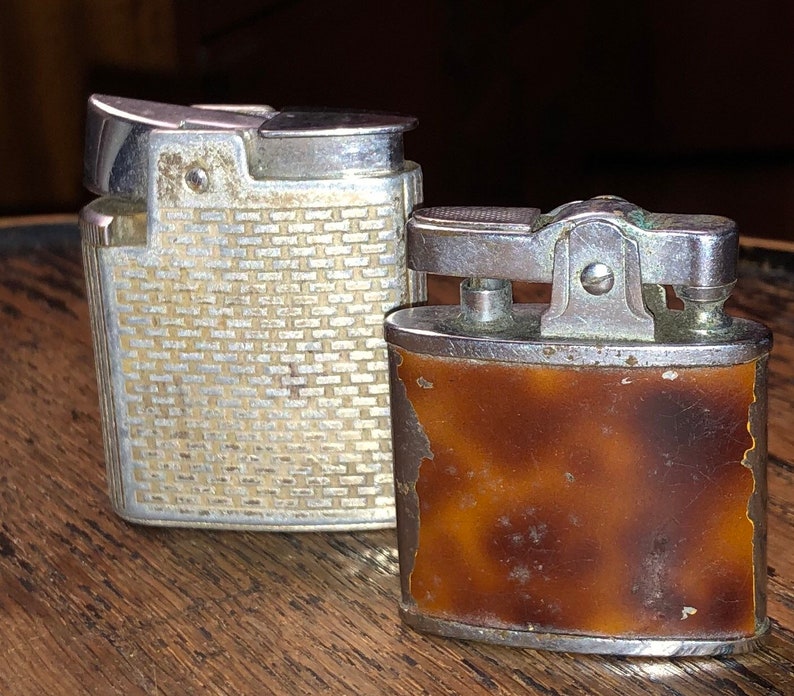 May include: Two vintage lighters, one silver with a textured design and one brown with a tortoiseshell pattern.