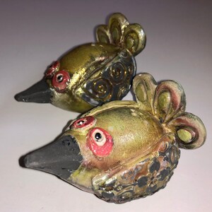 May include: Two ceramic bird figurines with black beaks, gold and green paint, and red and black eyes.