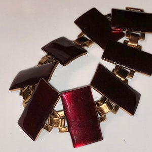 Peut inclure: Un bracelet en or et bordeaux avec un design g&eacute;om&eacute;trique. Le bracelet est compos&eacute; de maillons m&eacute;talliques avec des carr&eacute;s en &eacute;mail bordeaux.