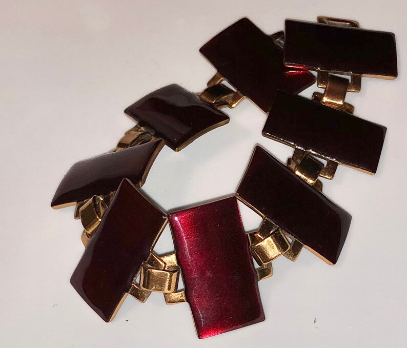 Peut inclure: Un bracelet en or et bordeaux avec un design g&eacute;om&eacute;trique. Le bracelet est compos&eacute; de maillons m&eacute;talliques avec des carr&eacute;s en &eacute;mail bordeaux.